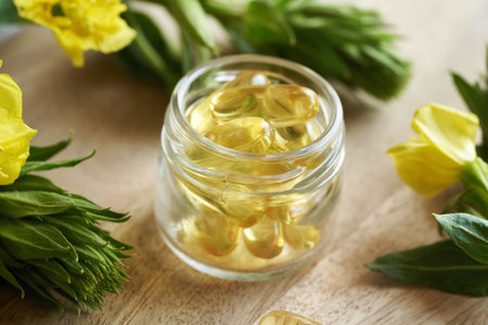 A glass bottle containing gel capsules of evening primrose oil with blooming Oenothera biennis plant. Nutritional supplement.の写真素材