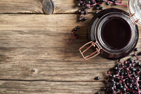Homemade black elder syrup with fresh elderberries on wooden background with copy space, top view