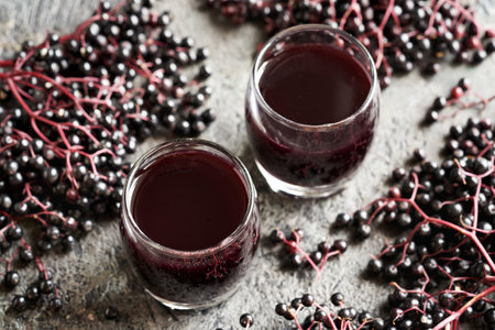 Two glasses of black elderberry syrup with fresh berriesの写真素材