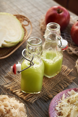 Two bottles of green cabbage and cucumber juice with fresh red apples on a tableの写真素材