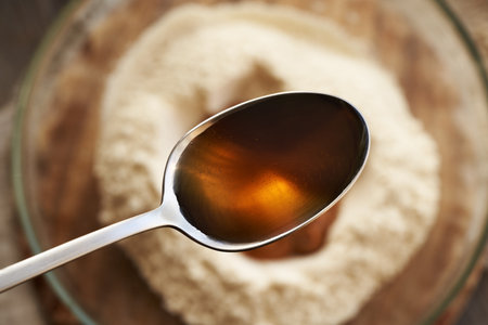 A spoon of maple syrup above a bowl of whey protein powder and peanut butter - preparation of homemade protein chocolate barsの写真素材