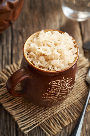 Homemade fermented cabbage or sauerkraut in a brown cup on a wooden tableの写真素材