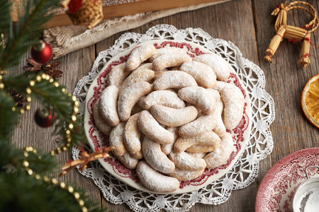 Homemade Christmas cookies called Kipferl or vanilla crescents coated in sugar on a plate with decorated fir tree, top viewの写真素材