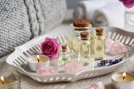 Bottles of aromatherapy essential oil with lavender and rose flowers, rose quartz stones, candles and spa towelsの写真素材