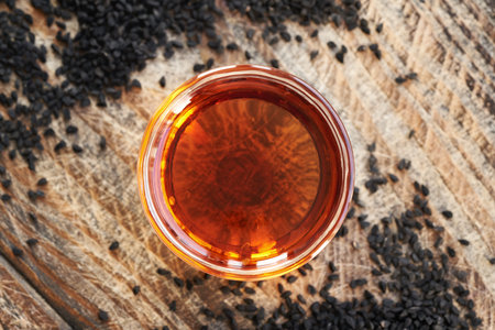 Black cumin or Nigella sativa seed oil in a glass bowl, top view. Healthy anti-inflammatory and...