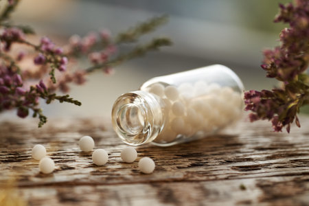 A bottle of white homeopathic pills or globules spilled on a table with pink dried flowersの写真素材