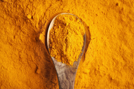 Ground turmeric root powder on a wooden spoon, top view
