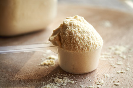 Whey protein powder in a plastic measuring spoon on a wooden tableの写真素材