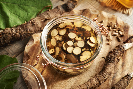 Making homemade herbal tincture from fresh sliced burdock root and alcohol in a glass jar on a tableの写真素材