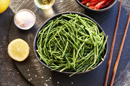 Green Salicornia seaweed in a bowl with salt, lemon, sesame seeds and chilli peppers on dark background`の写真素材