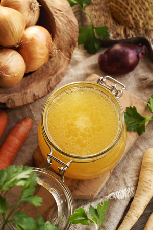 Chicken bone broth in a glass jar with fresh root vegetablesの写真素材