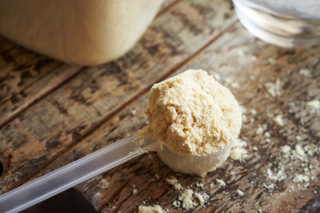 Whey protein powder in a transparent measuring spoon on a wooden tableの写真素材