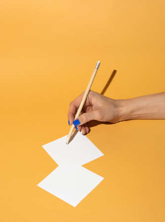 Pencil in woman hand who write notes on orange background.. Minimal business concept.の写真素材