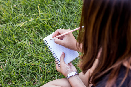 girl with pen writing on notebook on grass outside.の写真素材