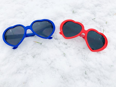 two Heart Shaped sun glasses bright blue and red on snow background winter valentines wedding loveの写真素材