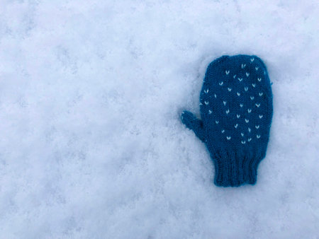 One blue knitted heart pattern baby child glove on snow background isolatedの写真素材