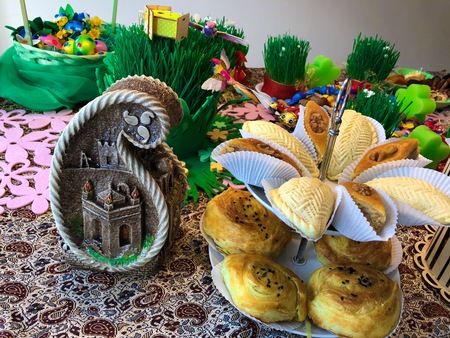 Novruz setting table decoration, tea in tulip shape glass on ethnic motives rustic table cloth with wheat grass, dyed eggs, traditional sweets, samovar, new year sring celebration, nature awakening orchids birds macronsの写真素材
