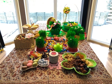 Novruz setting table decoration, tea in tulip shape glass on ethnic motives rustic table cloth with wheat grass, dyed eggs, traditional sweets, samovar, new year sring celebration, nature awakening orchids birds macronsの写真素材