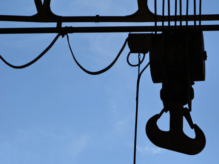 Industrial hook viewed from below. Backlit shot - Blue sky background. Yard area.