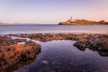 Alcudia lighthouse ( Faro De Alcanada) Located near Alcudia beach (playa de alcudia) and Alcudia Town. Small island with rocks in clear sea with beautiful blue sky and white clouds. Alcudia, Mallorca, Spain.の写真素材