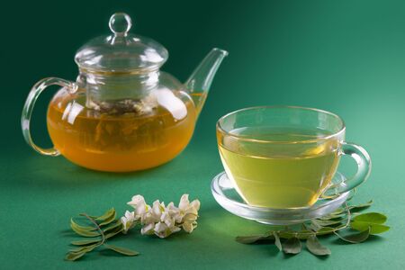 Flowers of acacia and Acacia tea in transparent tea pot and cup on green plain backgroundの写真素材