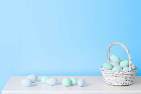 Basket with pastel blue and turquoise Easter eggs on white table near blue wall. Minimal Easter...