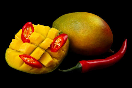 Diced half of mango, hot chili pepper rings, whole red hot pepper and whole mango on pure black background. Ingredients for salsa.の写真素材