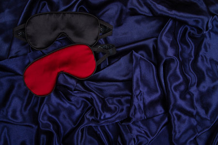 Two silk sleep mask lie on dark blue silken background. Horizontal banner with negative space for copy placementの写真素材