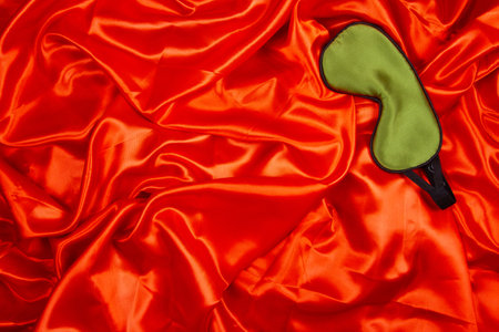 Green silk sleep mask lie on bright red silken background. Horizontal banner with negative space for copy placementの写真素材