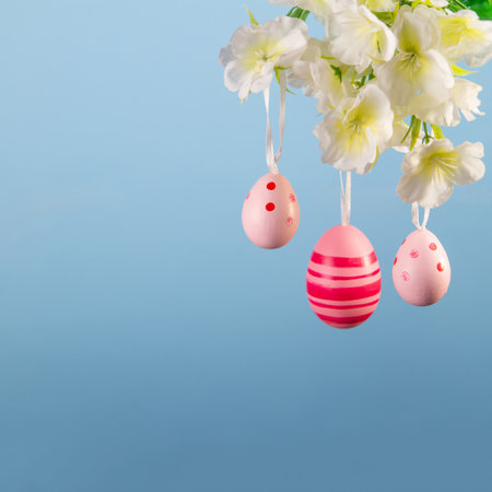 Charming spring scene of pink Easter eggs swaying gently from a budding branch on a serene blue backgroundの写真素材