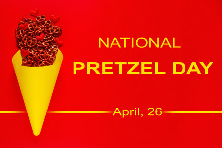 Mini pretzels and small colorful hearts in yellow paper cone lie on red background. National Pretzel day concept observed on April 26の写真素材