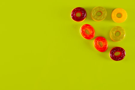 Triangle of round jelly candies at the corner of yellowish green background. Bright display of sugar circlesの写真素材