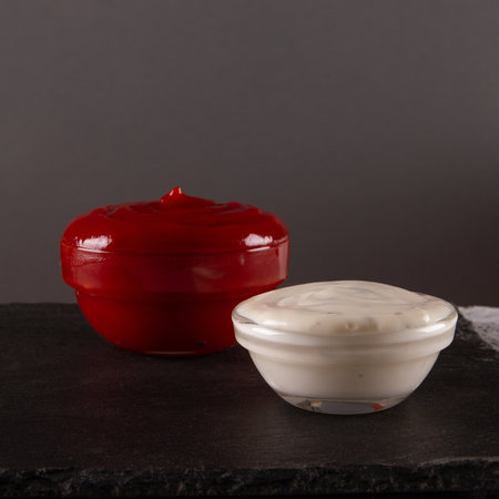 Red and white dipping sauces on black slate serving board with blank space. Savory contrast.の写真素材