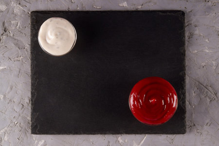 Red and white dipping sauces on black slate serving board with blank space. Saucy sensation.の写真素材