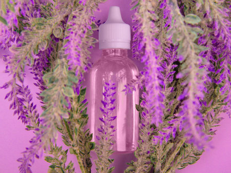 Liquid aroma extract in transparent bottle lie among purple flowers on violet backgroundの写真素材