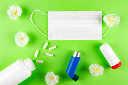 White shurgary mask, white flowers, bottle with pills and inhalers on light green background. Allergic bronchial reaction Conceptの写真素材