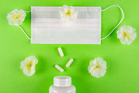 Striking juxtaposition of face mask and handful of capsule pills against green backdrop with beautiful flowers, underscoring the need for balance in our approach to health and well-being.の写真素材