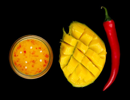 Top view of sweet mango chili sauce, diced half of mango and whole red hot pepper on black backgroundの写真素材