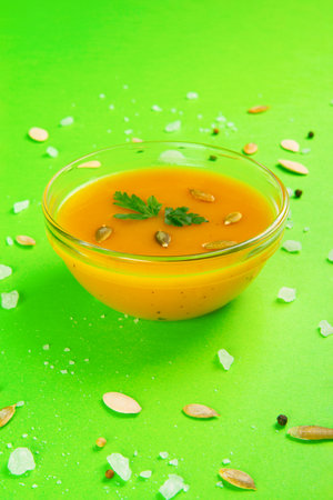 Autumn Vegetarian pumpkin and carrot cream soup on Vibrant emerald backdropの写真素材