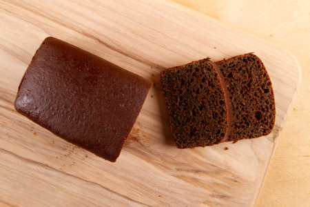Dark bread displayed in loaf and sliced form, against light beige wooden backdropの写真素材