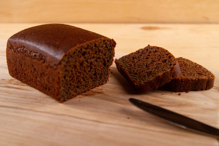 Light beige wooden base highlighting loaf and slices of dark bread. selective focusの写真素材