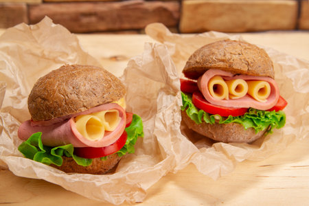 Appetizing sandwiches with ham, cheese and fresh lettuce served on baking paper on wooden table backgroundの写真素材