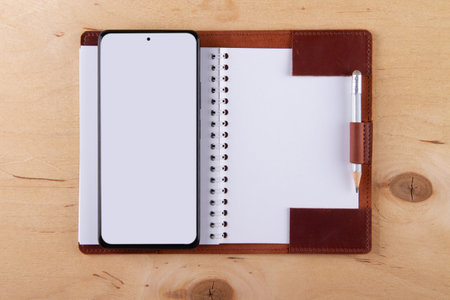 Digitalization concept. Paper notebook vs smartphone. Digital phone with blank white screen and empty drawing block lie on wooden tableの写真素材