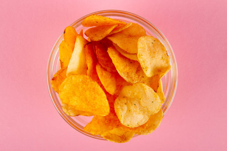Potato chips in glass bowl isolated on pastel pink background. top view