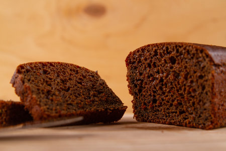 Dark bread loaf and its sliced counterparts arranged on light beige wooden backgroundの写真素材