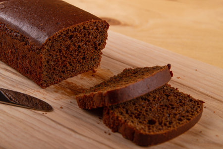 Loaf and sliced portions of dark bread positioned against light beige wooden backgroundの写真素材