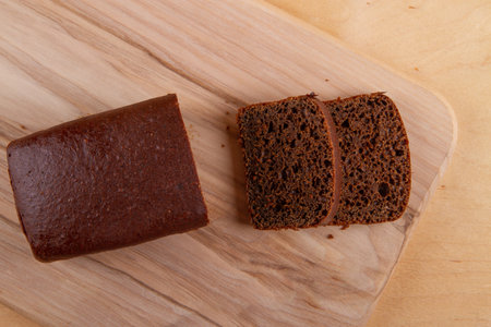 Loaf and slices of dark bread on light beige wooden backgroundの写真素材