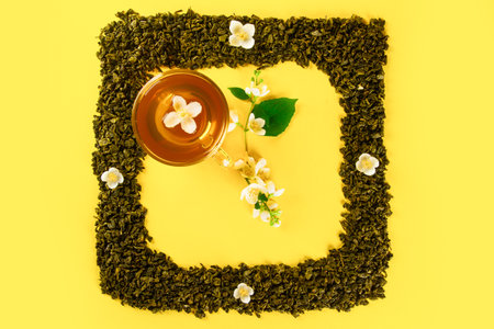 Mockup of dried tea leaves and fresh jasmine flowers shaped in square clock Frame with tea cup in center and jasmine branches point to five o'clock isolated on plain light yellow backgroundの写真素材