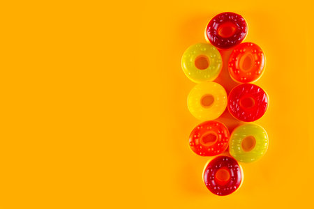 Few jelly candies in the shape of donut lie on light orange background. Bold surface for sweet circular confectionsの写真素材