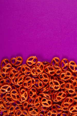 Border of mini pretzels on purple background. Vibrant color backdrop with savory twistsの写真素材